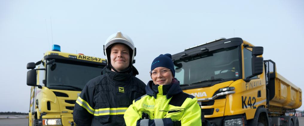 Kaksi työntekijää seisoo isojen ajoneuvojen edessä.