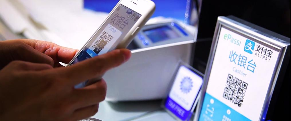 Passenger scanning Alipay QR-code with a smartphone at cash register.