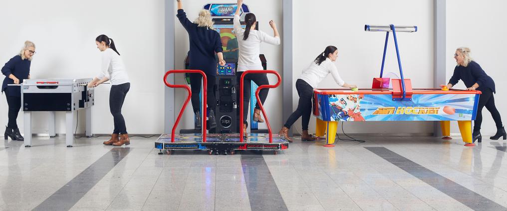 Kaksi henkilöä kokeilee eri arcade pelikoneita Helsinki-Vantaan lentoasemalla.