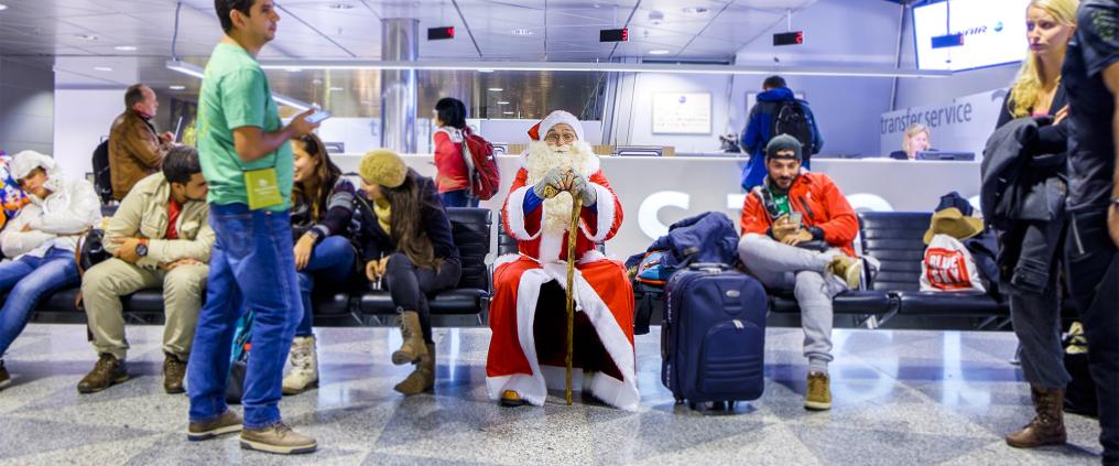 Santa Claus waiting for a flight at the gate with other passengers.