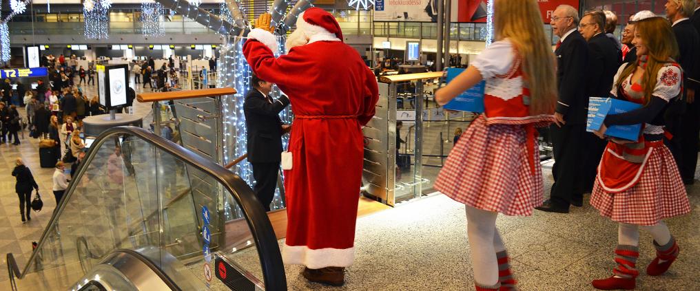 Joulupukki vilkuttaa matkustajille kuoron laulaessa hänen vieressä.