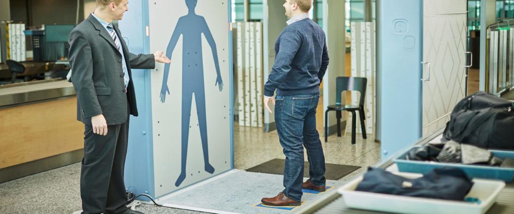 A man standing at a body scanner at airport security.