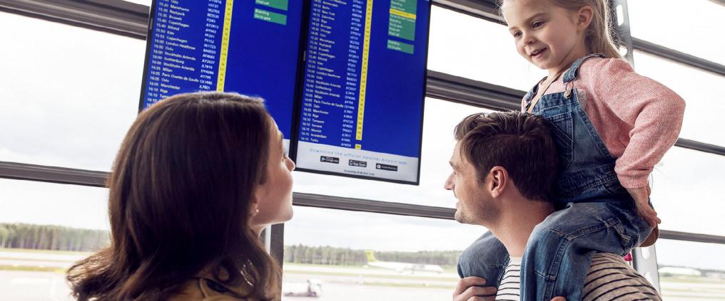 Family of three looking for their flight from flight departure timetable display. 