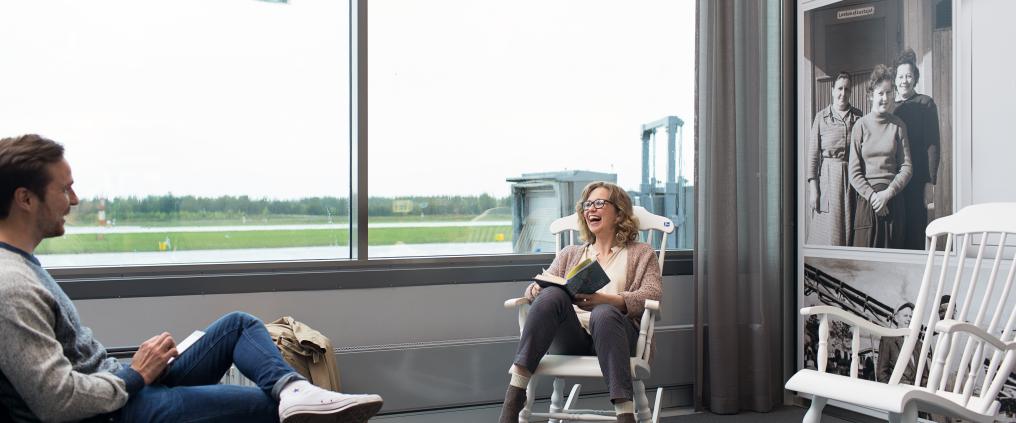 Hyväntuuliset matkustajat rupattelevat keskenään, toinen heistä istuu keinutuolissa kirja sylissään.