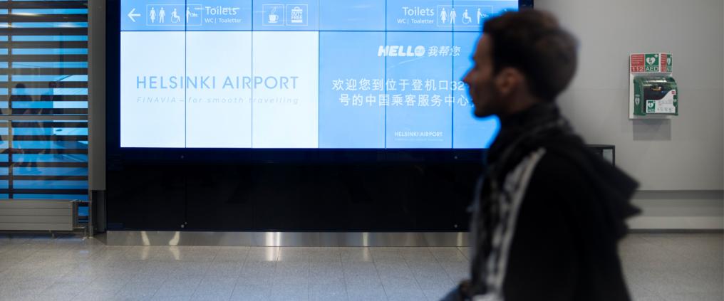 Passenger walking past signs at airport terminal.