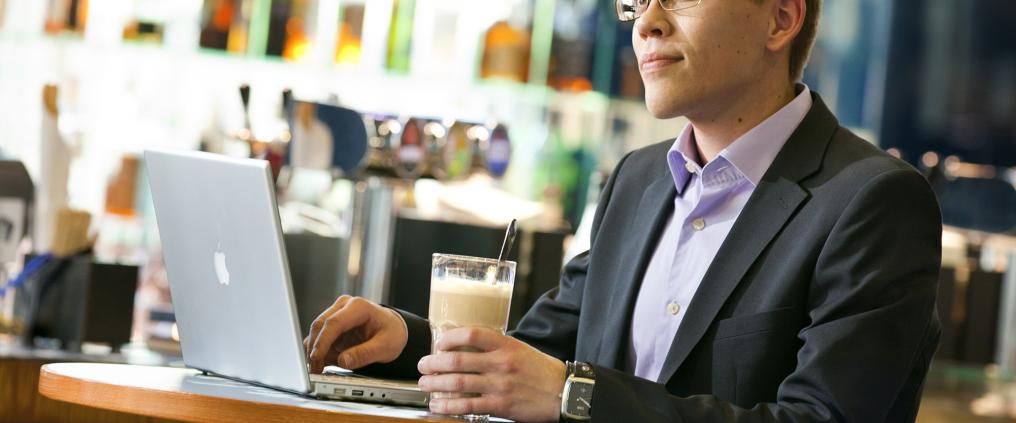 Mies käyttää kannettavaa tietokonetta kahvilassa.