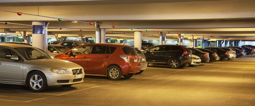 Multiple of cars parked in a lit parking hall.