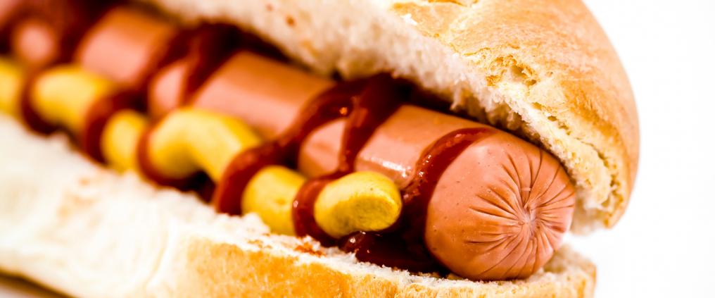 Lähikuva hot dogista, jossa on ketsuppia ja sinappia.