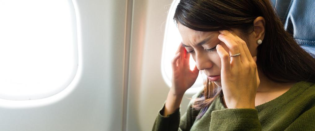Woman visibly in discomfort massaging temples on a plane.