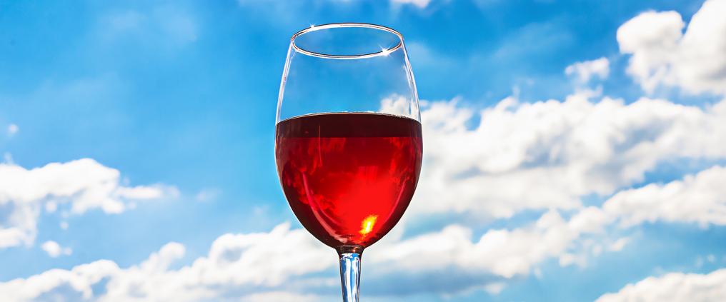 Wine glass with red wine and clear blue sky behind it.