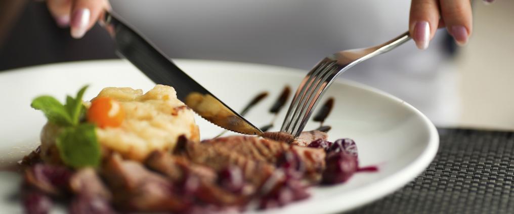 Closeup of hands holding knife and fork cutting steak to eat.