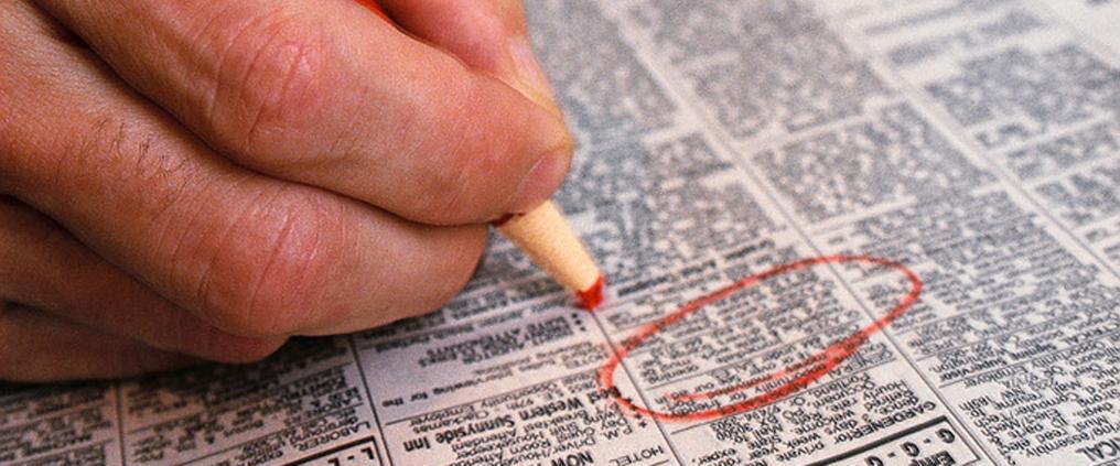 Käsi ympyröi kynällä työpaikkailmoituksen sanomalehdestä.