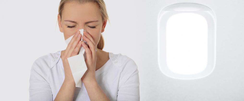 Woman blows her nose with a tissue inside airplane cabin.