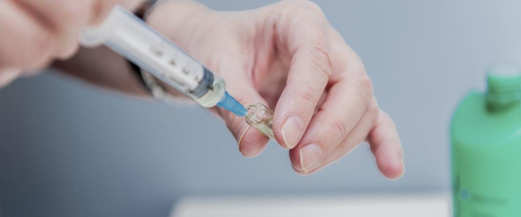 Hands drawing up medicine from a vial with syringe.