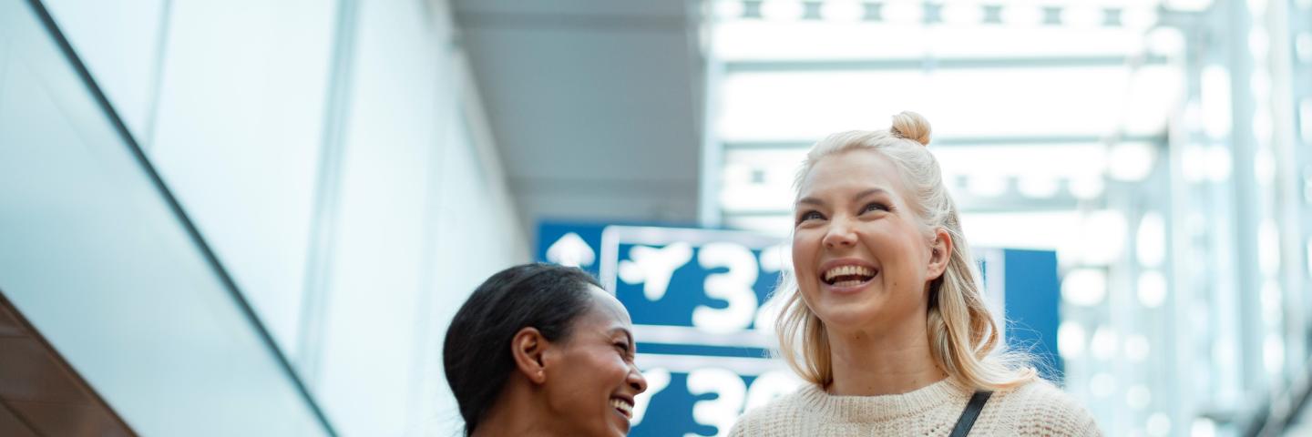 Kaksi henkilöä nauraa hyväntuulisena lentoasemalla.