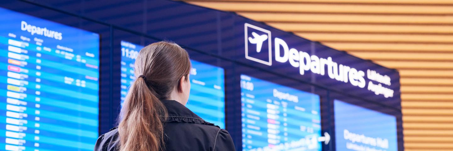 Ihminen seisoo selkä kohti kameraa ja katsoo digitaalista lentotietonäyttöä.