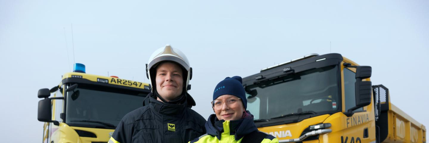 Kaksi työntekijää seisoo isojen ajoneuvojen edessä.