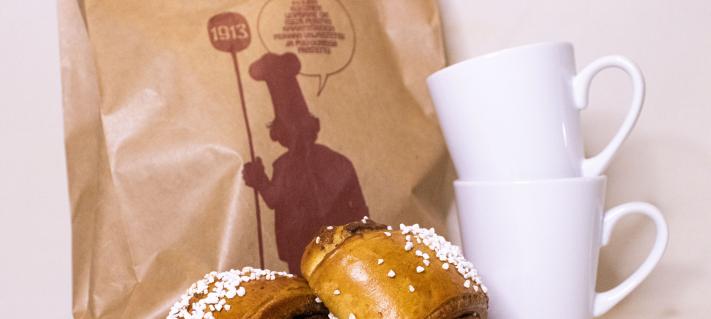 Kuvassa kahvimukeja, pullaa ja paperipussi.