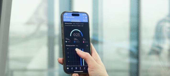 Käsi pitelee puhelinta, jonka näytöllä on AOS-järjestelmän mittareita.