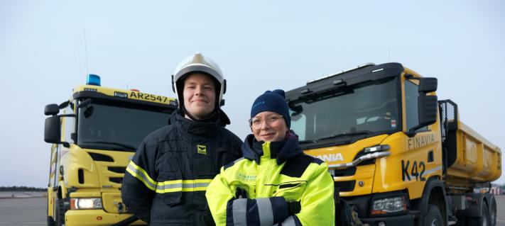 Kaksi työntekijää seisoo isojen ajoneuvojen edessä.